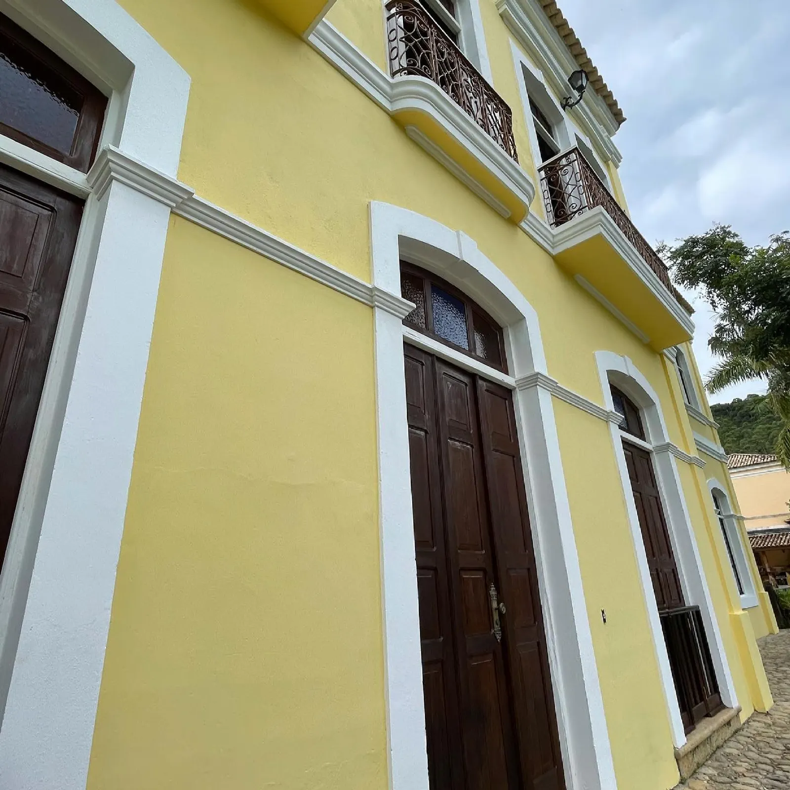 Fachada amarela do casarão histórico da Fazenda Neuchatel, com molduras brancas, arcos e sacadas de ferro