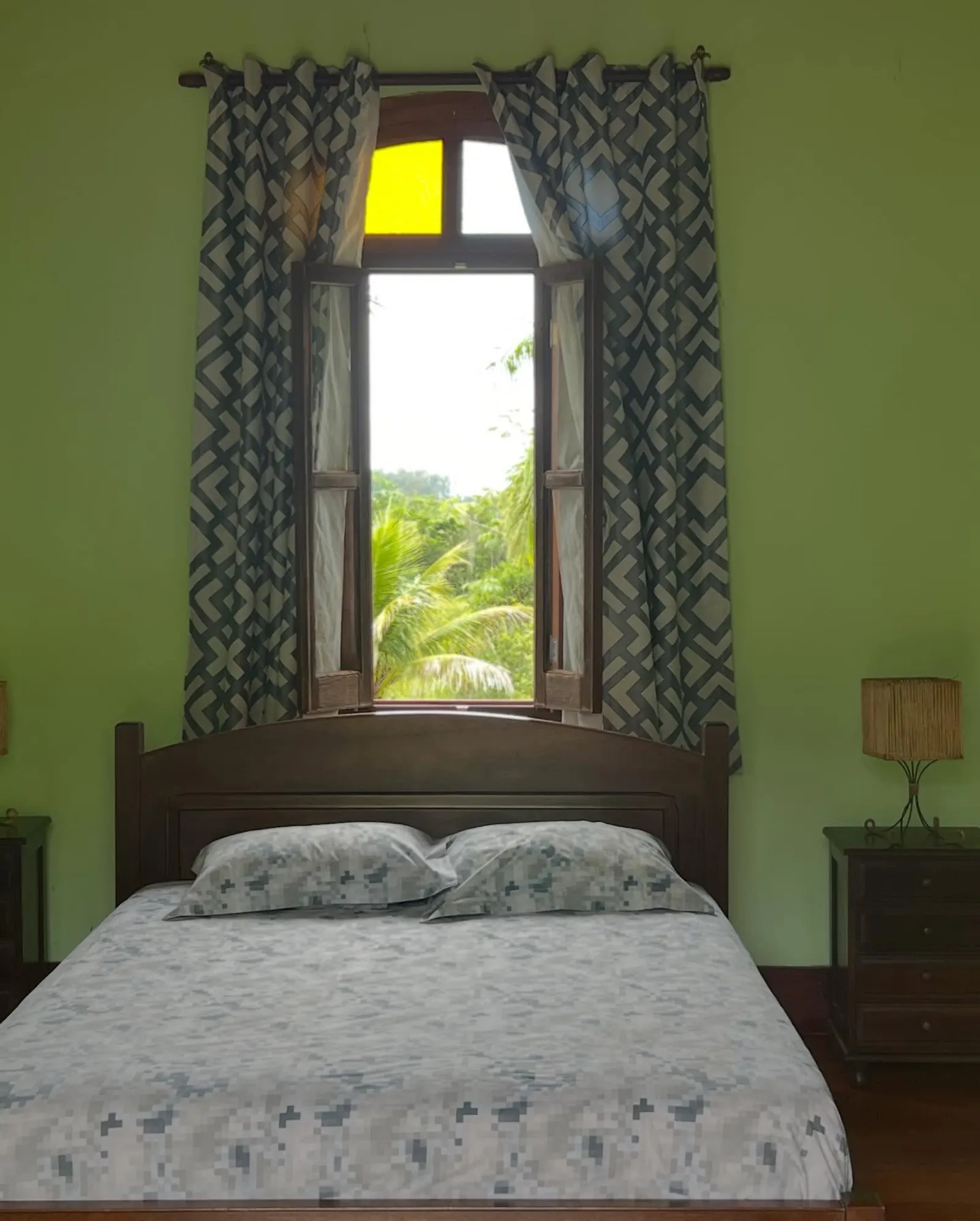 Quarto de hospedagem da Fazenda Neuchatel com cama de casal e janela em arco aberta para a mata